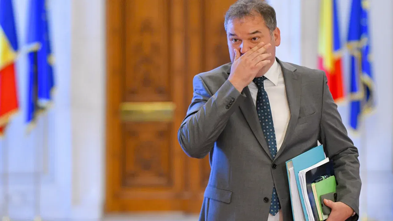 Cseke Attila, ministru interimar al Sănătății, într-o clădire oficială, cu drapelele României și Uniunii Europene în fundal.