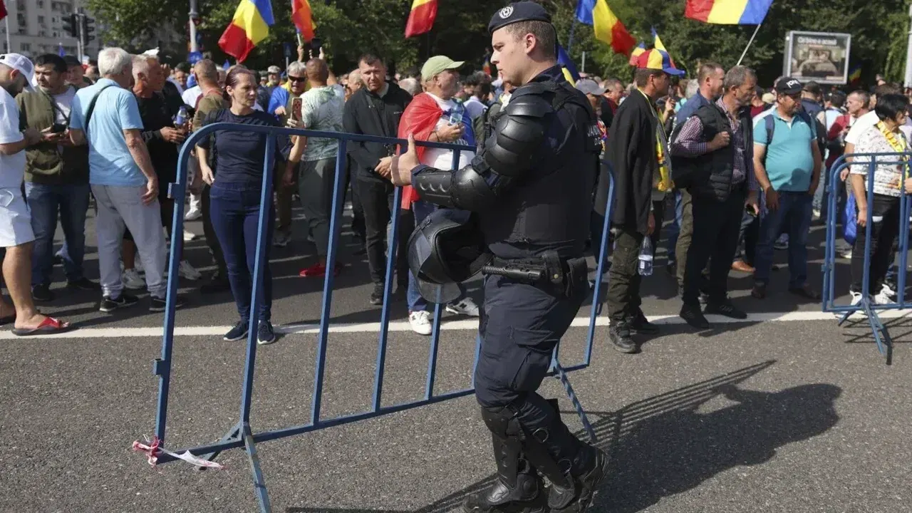 Jandarm mutând un gard metalic în fața protestatarilor cu steaguri ale României, în Piața Victoriei