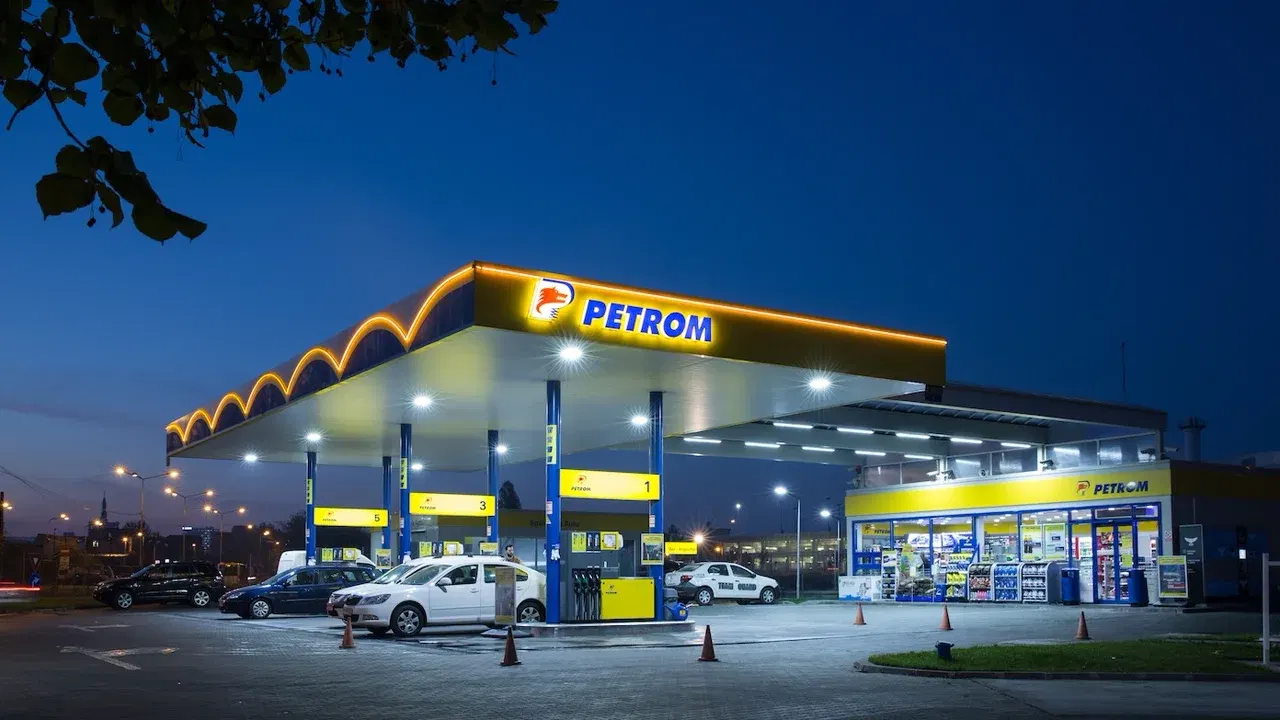 Stație Petrom luminată seara, cu pompe de carburanți și mașini la alimentare