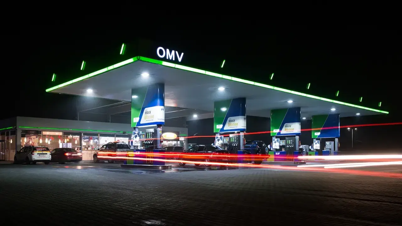 Stație OMV luminată noaptea, cu pompe de carburant și autoturisme
