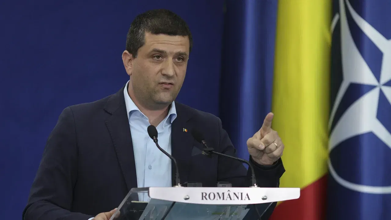 Radu Miruță vorbește la un pupitru, cu drapelele României și NATO în fundal